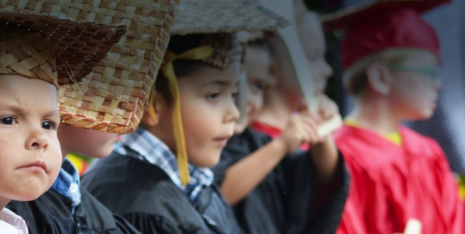 Children in a graduation ceremony wearing robes and mortar boards.