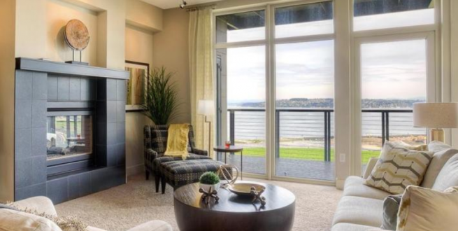 Image of a furnished living room with pastel colors and large windows.