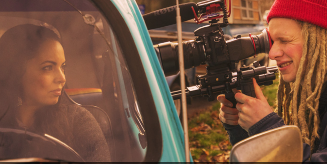 Cameraman filming a woman in a vehicle.