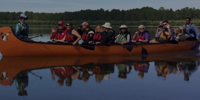 People rowing a canoe together, in calm waters.